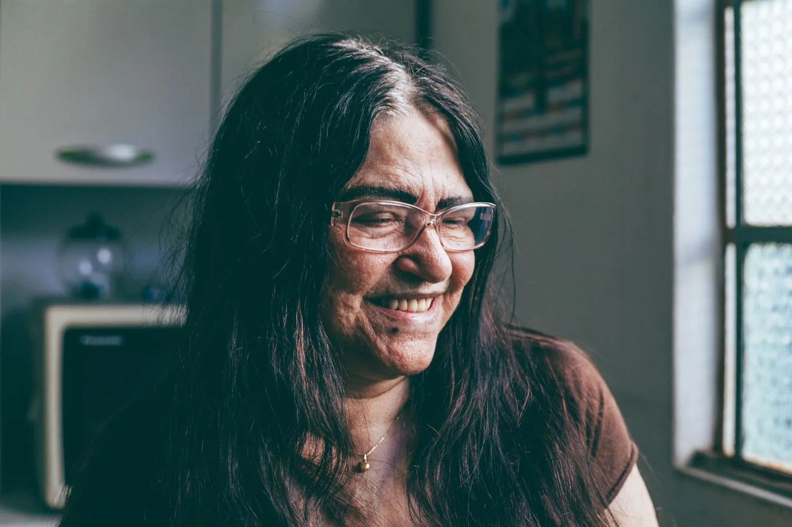 An older woman at home, content by a sunlit window.